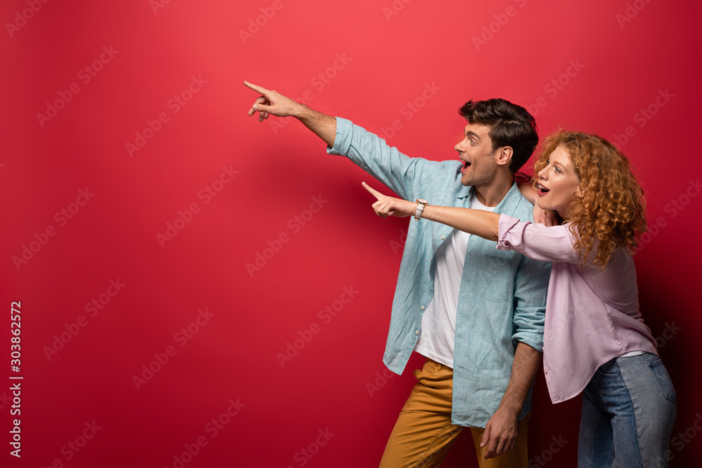 Εκτύπωση καμβά beautiful excited couple in casual clothes pointing isolated on red