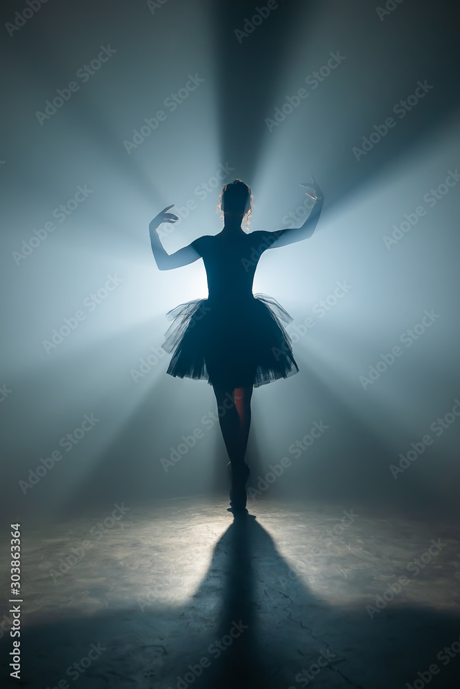Solo performance by ballerina in tutu dress against backdrop of luminous neon spotlight in theater. Silhouette of woman in pointe shoes dancing classical movements.
