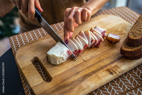 Obraz na płótnie lard of pig on wooden cutting board, big knife in female hand in the kitchen w salonie