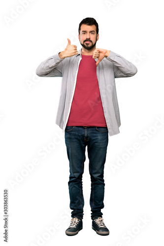 Full-length shot of Handsome man with beard making good-bad sign. Undecided between yes or not over isolated white background