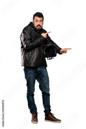 Full-length shot of Biker man frightened and pointing to the side over isolated white background © luismolinero