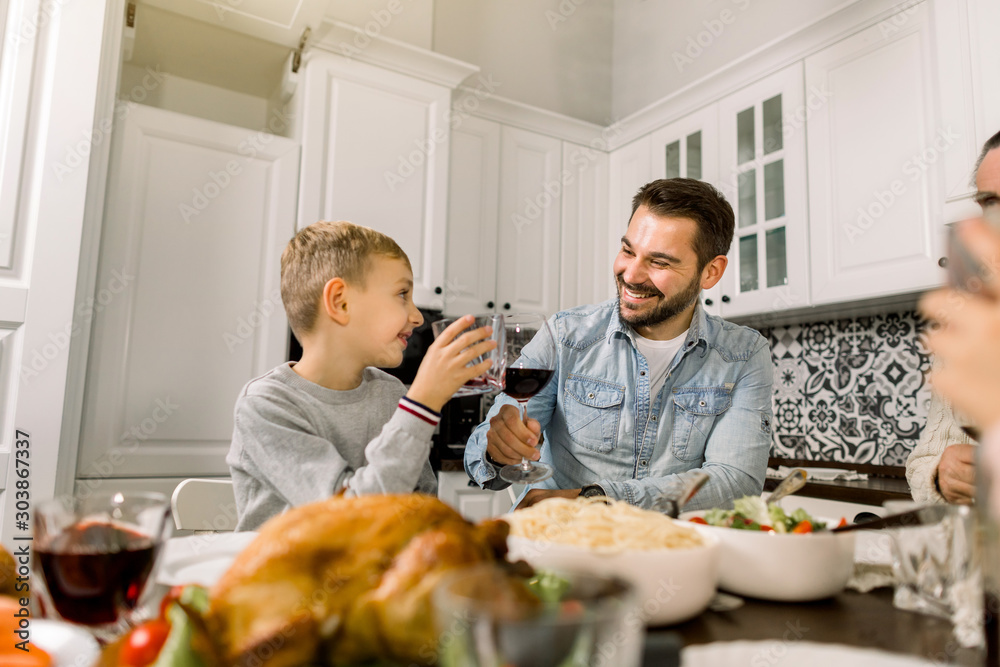 Family Enjoying Thanksgiving Meal At Table. Handsome father and little son clinking glasses with wine and juice and smiling Family Enjoying Thanksgiving Meal At Table. Handsome father and little son clinking glasses with wine and juice and smiling