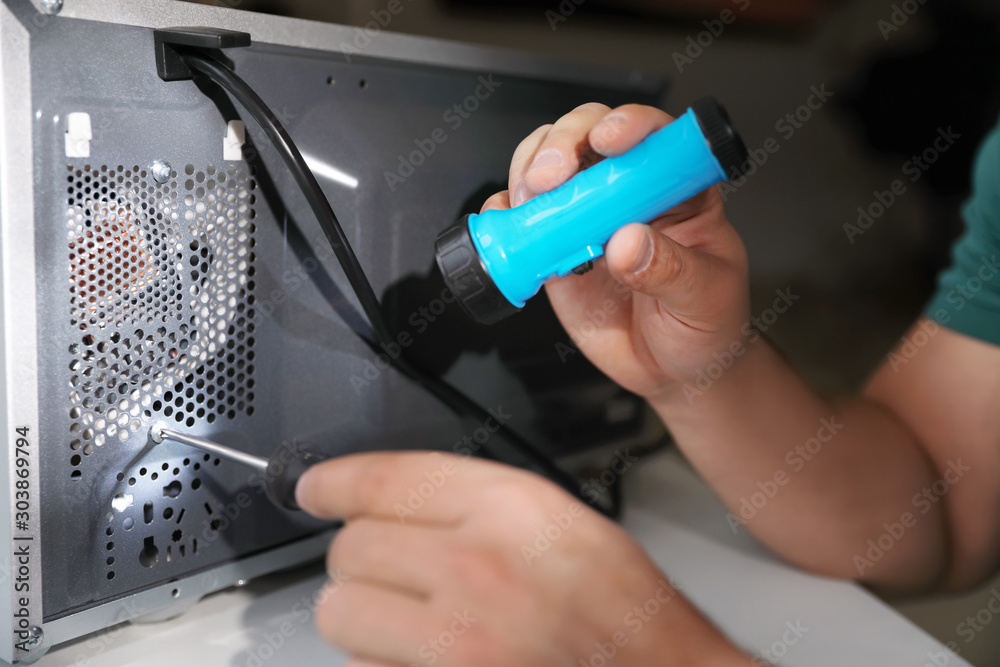 Repairman with flashlight fixing microwave oven indoors, closeup Repairman with flashlight fixing microwave oven indoors, closeup