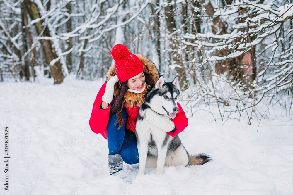 Young beautiful woman sitting with husky dog in the winter forest