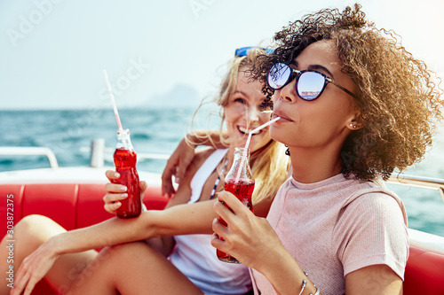 Wall Mural Two young female friends laughing over drinks on a boat
