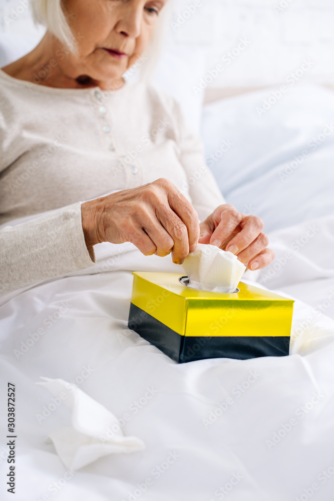 selective focus of ill senior woman taking napkin in bed