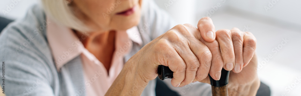 panoramic shot of senior woman with wooden cane in apartment