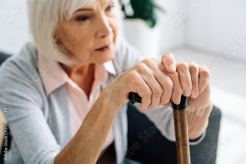 selective focus of senior woman with wooden cane in apartment