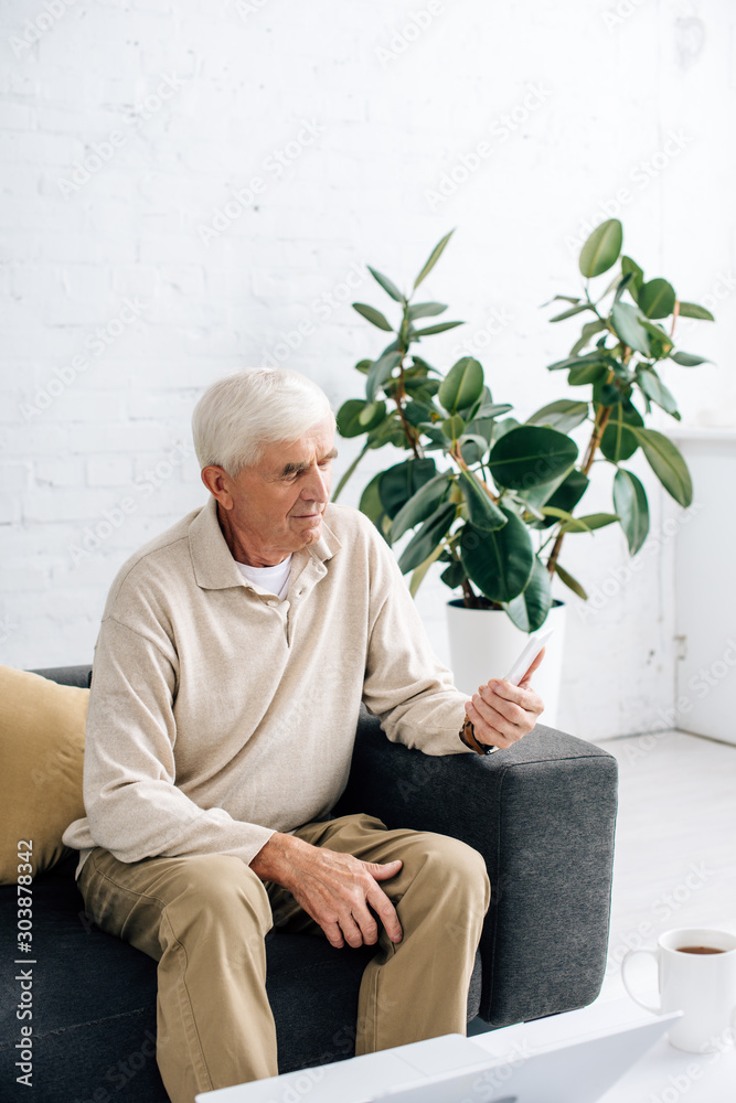 senior man sitting on sofa and using smartphone in apartment