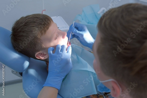 Dentist making fluoridation of child boy teeth after cleaning for protection. Doctor hygienist applying fluoride to teen teeth with brush. Covering teeth with fluoride gel in dentistry. Cure concept. photo