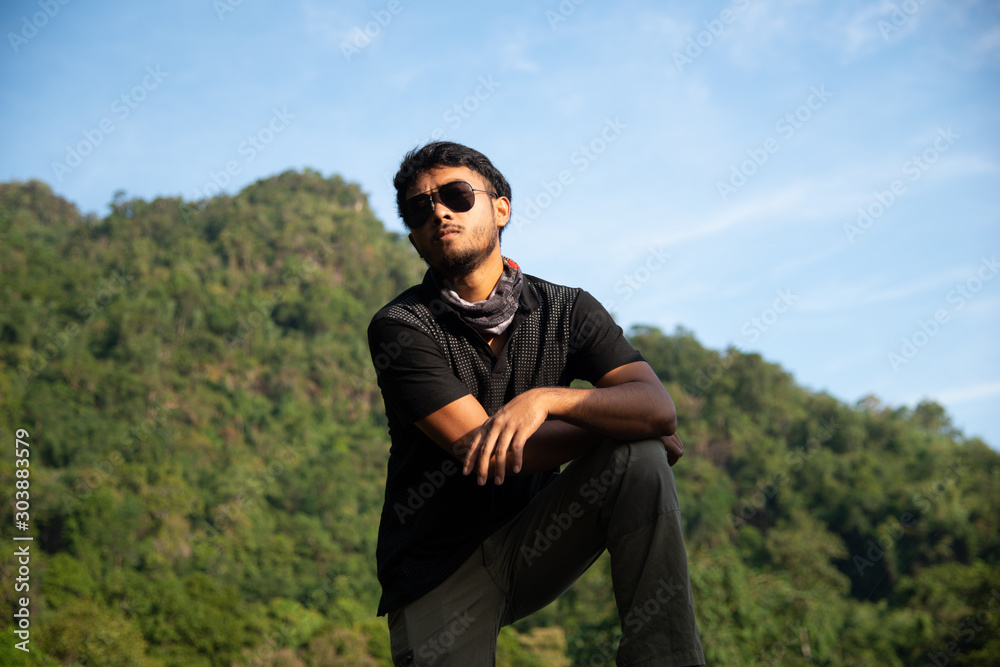 cool strong guy wear sun glasses posing at the cliff and looking up with green mountain view, solitude man with mountain cool strong guy wear sun glasses posing at the cliff and looking up with green mountain view, solitude man with mountain