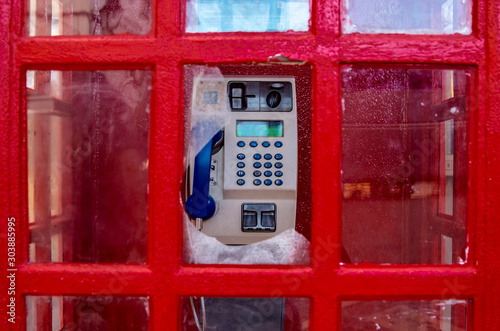 Tradycyjna czerwona budka telefoniczna, nowoczesny aparat telefoniczny, zbita szyba.