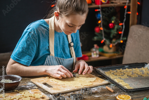 Young housewife makes dough for cooking festive ginger cookies. Cozy home atmosphere in the evening on Christmas eve