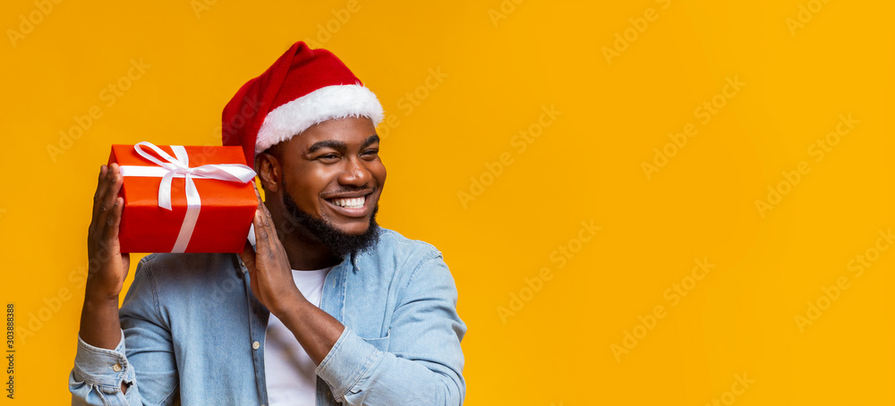 © Prostock-studio - Joyful black man in santa hat shaking christmas gift box