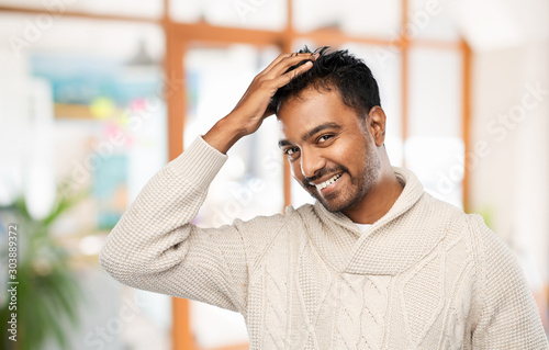 emotion, expression and people concept - smiling indian man in knitted woolen sweater touching his hair over office background © Syda Productions