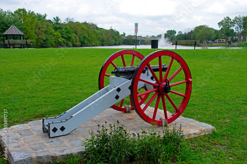 American Revolutionary War cannon with red wheels and a black barrel on display in front of a water fountain at Columbus Park, Piscataway, New Jersey,  photo