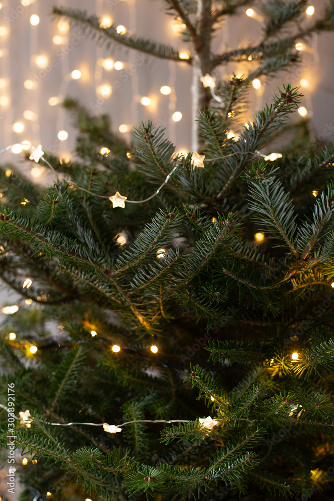 Christmas tree covered in lights on background of shiny garland on gray wall Christmas tree covered in lights on background of shiny garland on gray wall