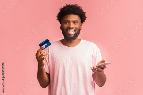 Happy man holding credit card, using cellphone for online shopping