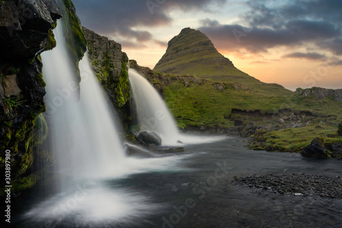 Kirkjufellsfoss and the famous mountain peak kirkjufell in the background while the sun sets. From snaefellsnes peninsula in the western part of iceland. Golden colors fills the sky.