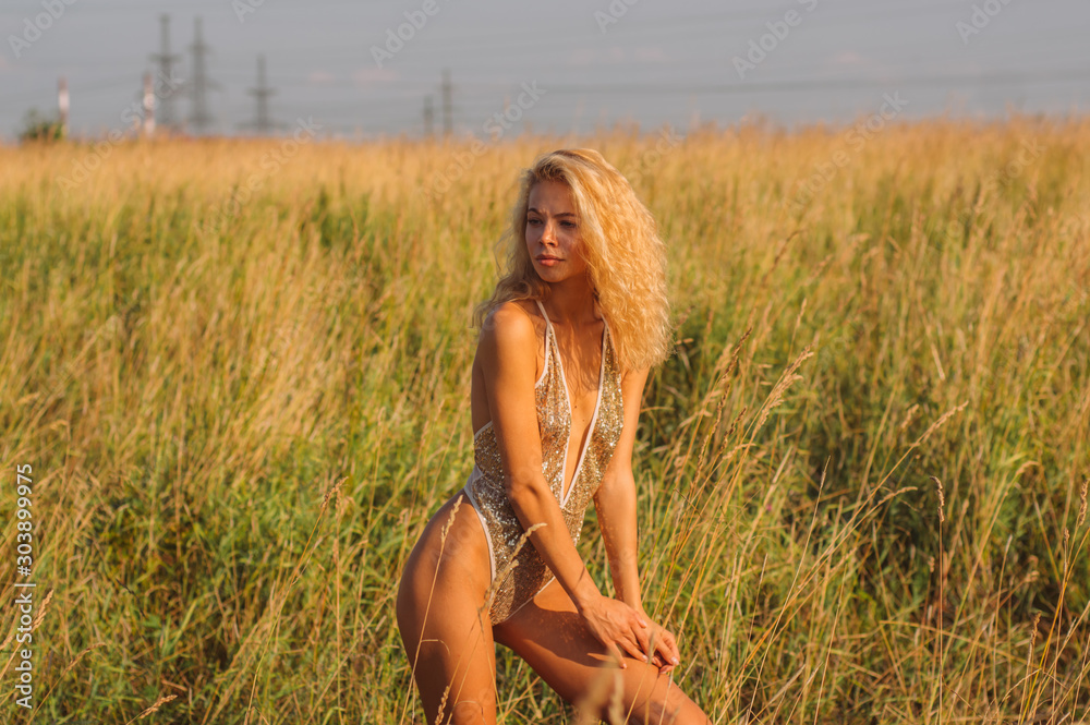 Φωτογραφία Young woman in golden glittering bodysuit walking among the field on sunset