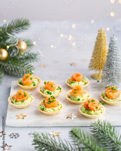 Canapes with smoked salmon, cream cheese and avocado on light background with space for text. Christmas and new year holidays background concept. Starters snacks recipe ideas.