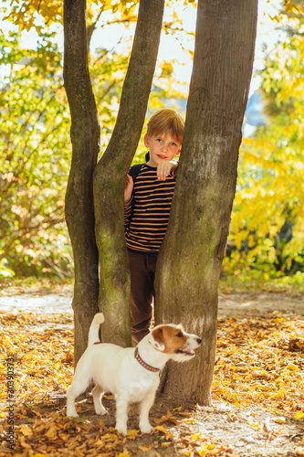 Vertical of blond boy caressing his dog Jack Russell Terrier playing, walking together after school outdoor at park in evening sunset beautiful light autumn season. True love friendship concept. © Iryna