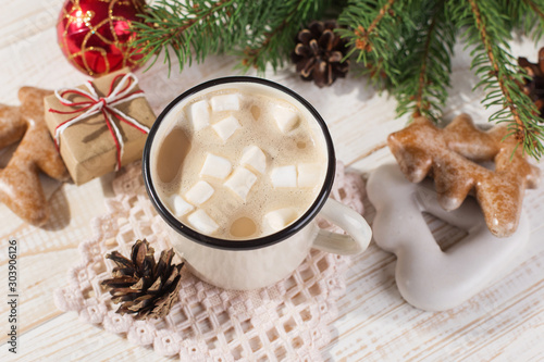 Hot Christmas drink with marshmallows in an iron mug and gingerbread cookies, on a white table. New Year, holiday background, copy space.