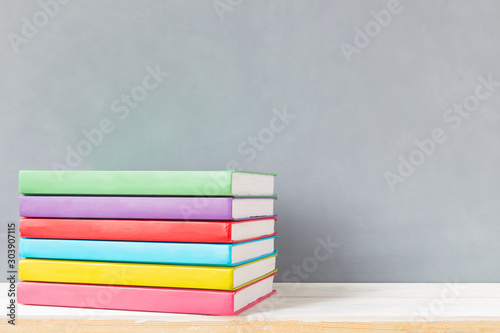 stack of multicolour books on a wooden shelf and gray wall. with copy space