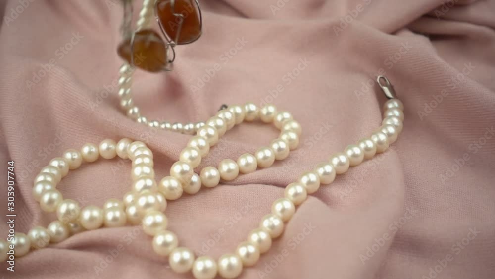 Falling jewelries on a pastel pink soft fabric in slow motion. Falling jewelries on a pastel pink soft fabric in slow motion.