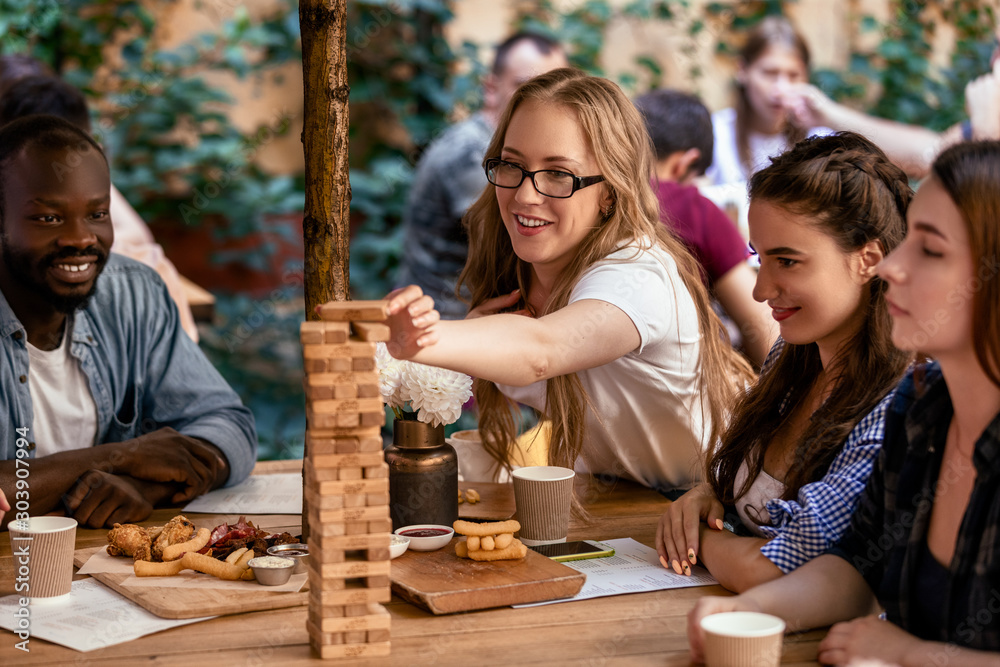 Φωτογραφία Caucasian girl is putting a brick to a tall tower at table game jenga at the res
