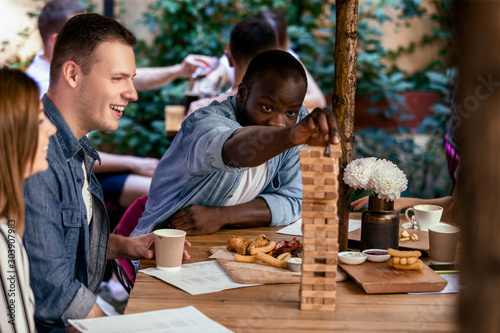 Fototapeta African boy is playing table game jenga with caucasian best friends at the local