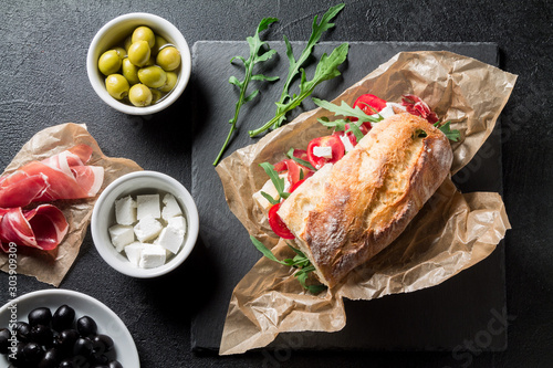 Sandwich with jamon, cheese, tomatoes and arugula on a black background