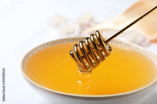 Bowl with organic honey and dipper on white background, closeup