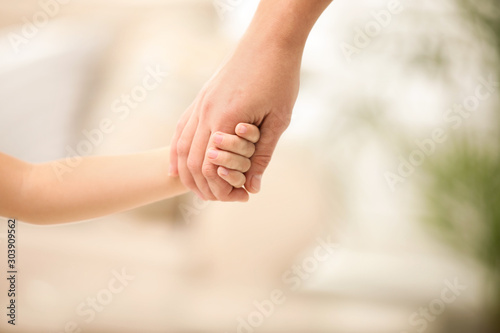 Mother holding hands with her child indoors, closeup. Happy family