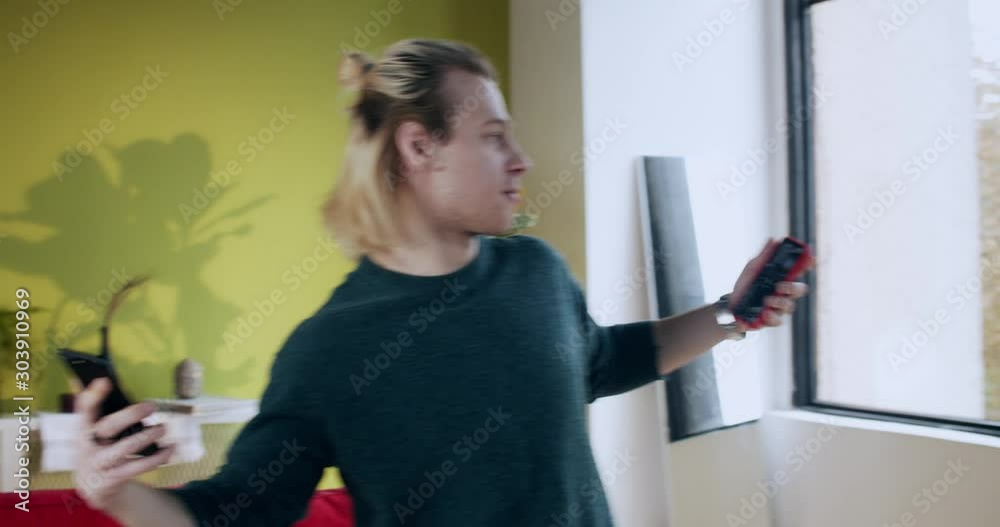 Happy excited young blonde man dancing with two smartphones celebrating online gambling victory and financial success having fun in home lounge. Happy excited young blonde man dancing with two smartphones celebrating online gambling victory and financial success having fun in home lounge.