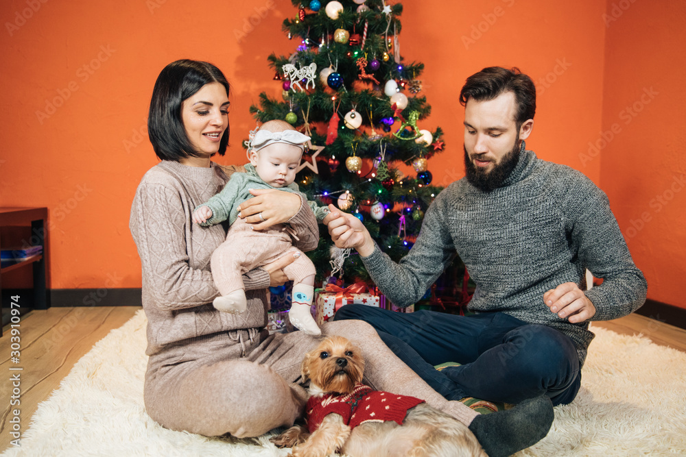 young family with a child near the Christmas tree, mom dad and their newborn daughter prepare for the New Year and Christmas, happy family young family with a child near the Christmas tree, mom dad and their newborn daughter prepare for the New Year and Christmas, happy family