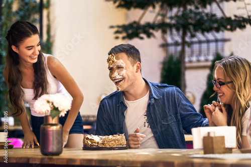 Принти на полотні Two caucasian girls and a guy with face diry  with cake cream are laughting and