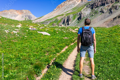 Open landscape view of green grass meadow field and back of man standing on trail to Ice lake near Silverton, Colorado in August 2019 summer on summit