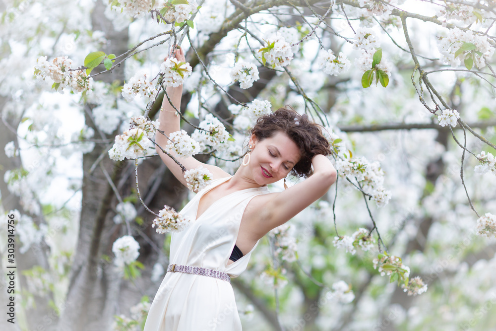 A portrait of beautiful young Caucasian woman with curly dark hair in blossoming orchard A portrait of beautiful young Caucasian woman with curly dark hair in blossoming orchard
