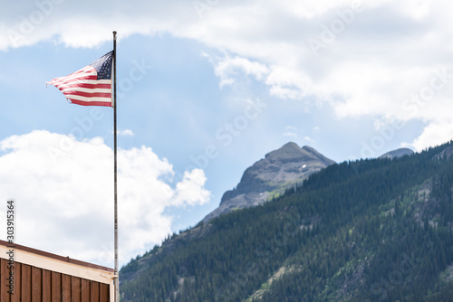 Flagpole on street in Silverton, Colorado summer with American flag waving in the wind and mountain peak in summer and blue sky clouds