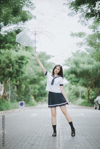 asian lady with short straight hair in Japanese student uniform holding an umbrella with arm raised posing on the street standing with pointed legs