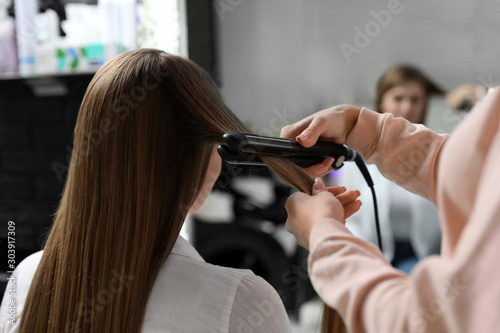 Hairdresser using straightener to style client's hair in salon