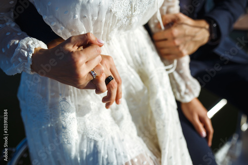 Bride and groom's hands with elegant wedding rings. Newlyweds hold hands with wedding ringson the background of sea and sun. Wedding details. Together. Wedding day. © maxbelchenko