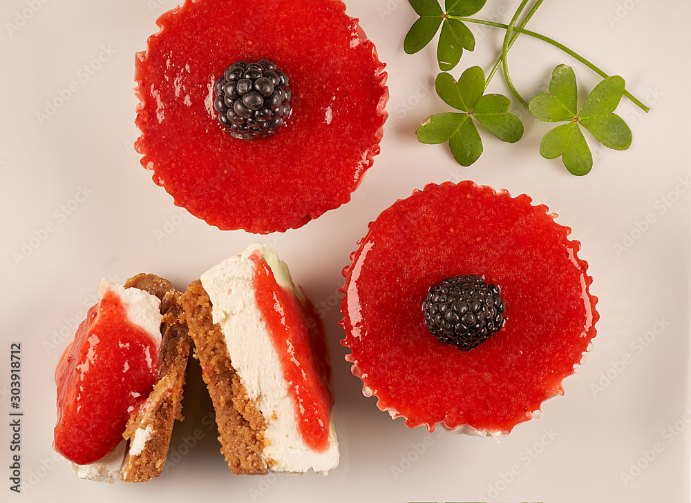 Φωτογραφία Aerial view and close-up of two homemade cheesecakes bathed in strawberry sauce and accompanied by another halved cheesecake and clover leaves on white background