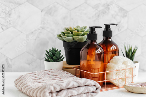 Soap and shampoo bottles and cotton towels with green plant on white table inside a bathroom background. photo
