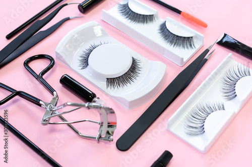Many different tools for eye lash extension on trendy pastel pink background. Creative knolling concept. Fake eyelashes, tweezers, brush and eyelash curler. Beauty pattern. Makeup cosmetics.