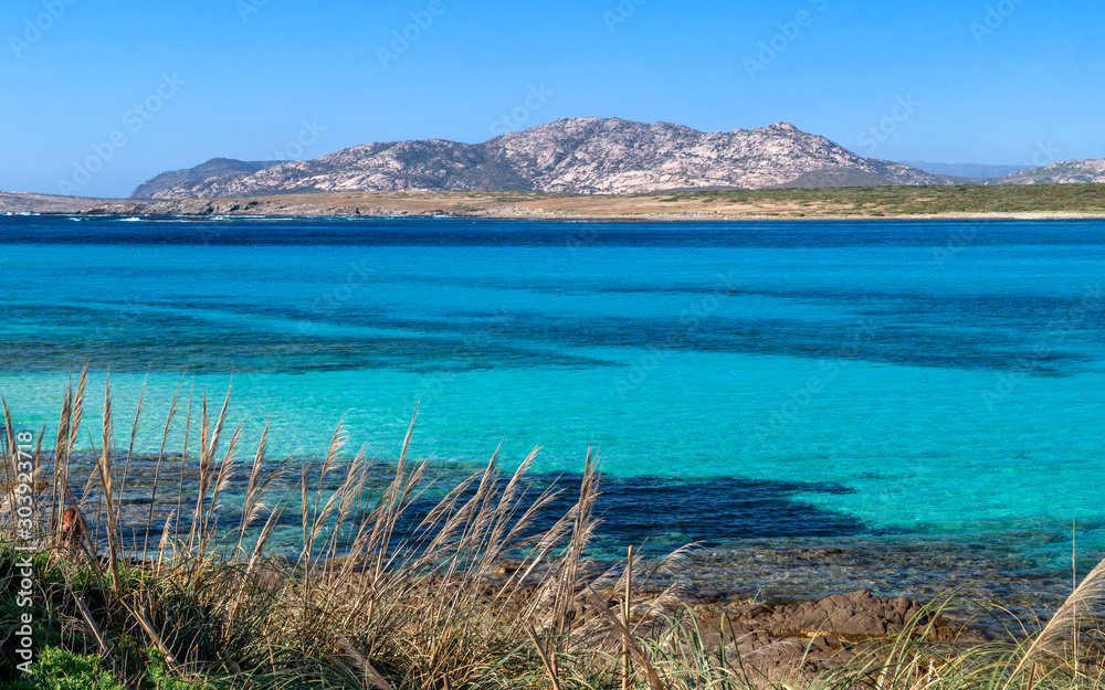 Panoramic view of La Pelosa beach in Stintino, turquoise clear water, mountains in the background. Sassari, Sardinia, Italy.