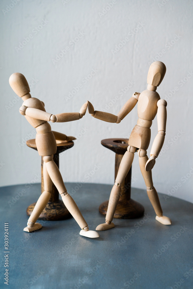 Two wooden human figures standing on a table shake hands. The concept of a positive greeting friends in a cafe at the tables Two wooden human figures standing on a table shake hands. The concept of a positive greeting friends in a cafe at the tables