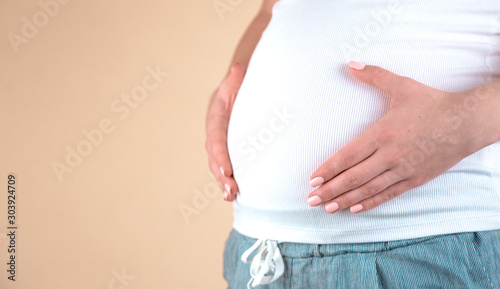 Authentic close up shot of an young pregnant woman in pajamas is caressing her belly just woke up in a bedroom in the morning.