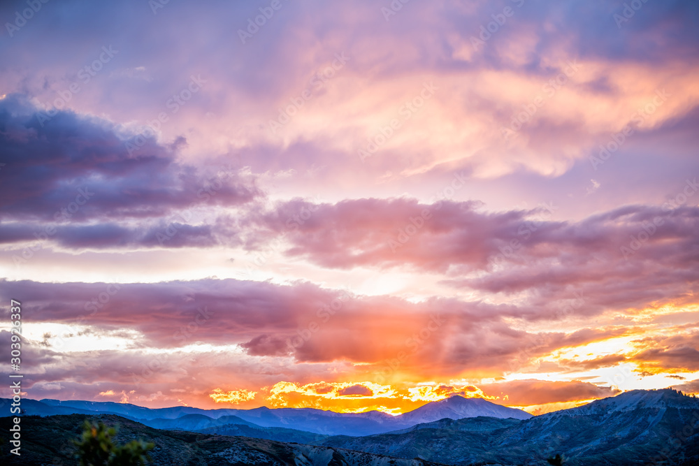 Fototapeta premium Orange purple cloudy sunset sun rays skyscape in Aspen, Colorado with rocky mountains peak and vibrant color of clouds at twilight with mountain ridge silhouette